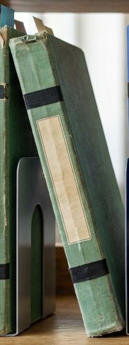 Digitally rendered: a worn, faded green notebook with a cream label leans against the one beside it, next to a steel bookend.
